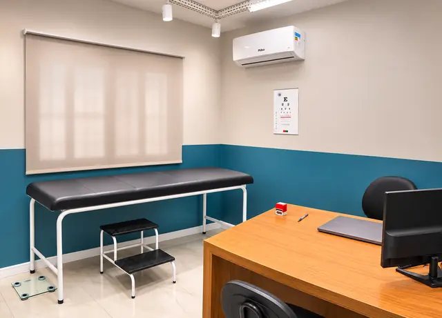 Consultório de exame clínico com maca, tabela de acuidade visual e mesa em madeira