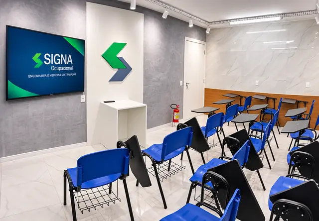 Sala de treinamentos com cadeiras universitárias azuis, TV e logotipo da Signa Ocupacional